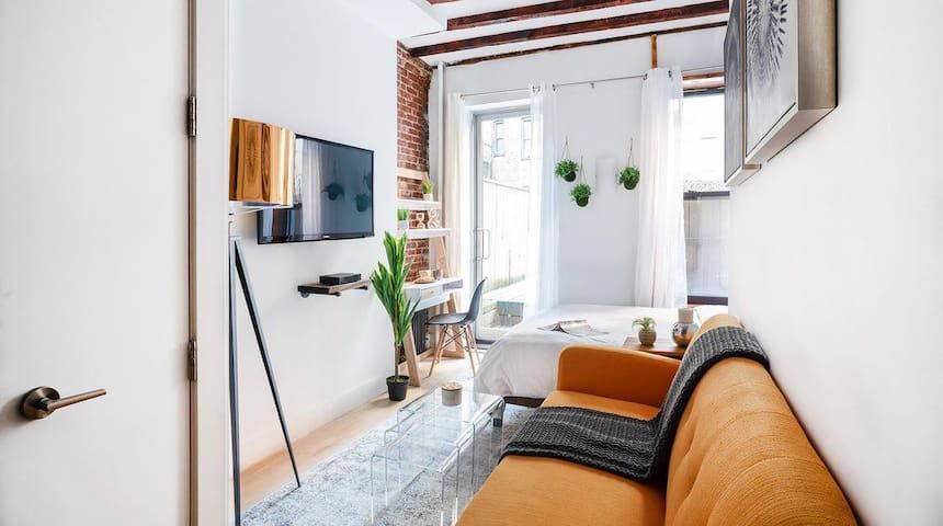 Studio apartment with orange chair, TV, brick wall, small terrace, and a washer and dryer. Located in Gramercy/Murray Hill.