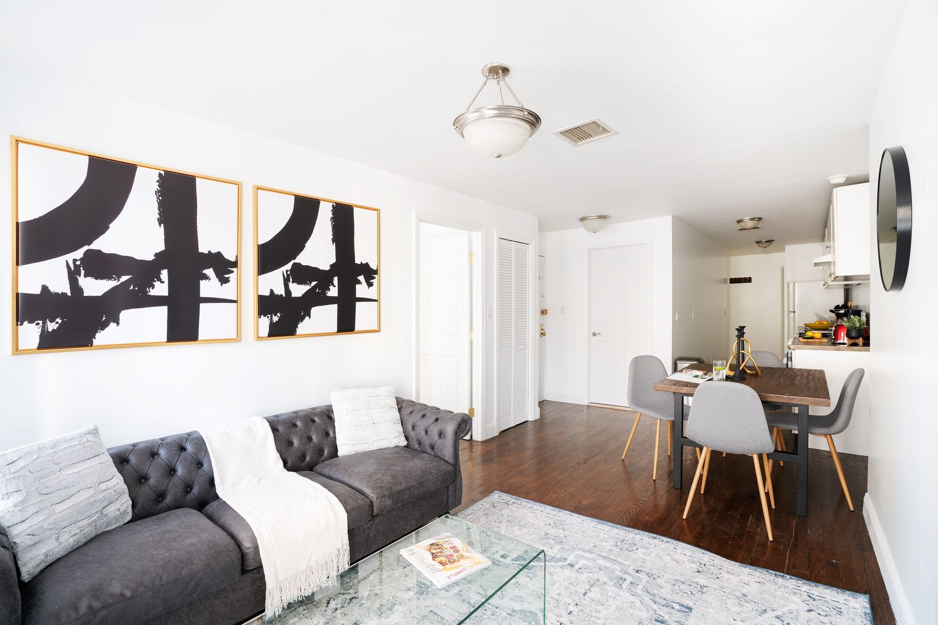 Modern three-bedroom apartment with a gray sofa, glass coffee table, abstract wall art, dining area with gray chairs, and a gray area rug. The apartment has a washer and dryer and is located in the Upper East Side.
