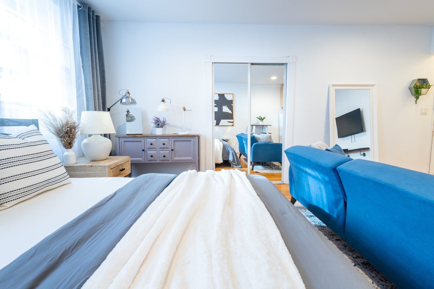 Modern studio apartment with a cozy bed, blue and gray accents, and a stylish dresser. Located in Gramercy/Murray Hill.