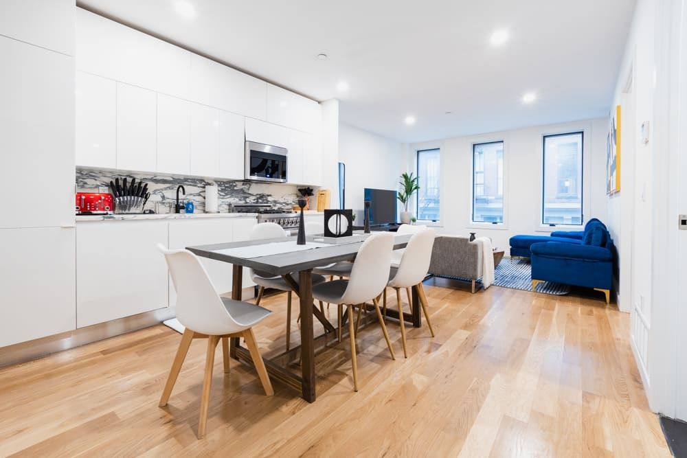 Modern 2-bedroom apartment in Union Square featuring a sleek white kitchen, a dark dining table with white chairs, and a living area with a blue sofa and large windows.