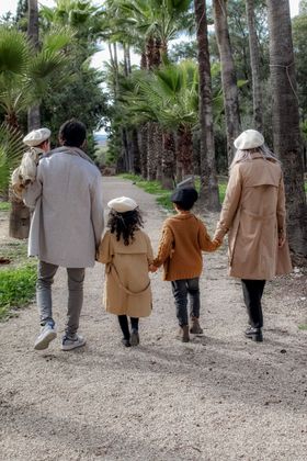 Quatre personnes s'éloignent sur un chemin de gravier boisé, entourées de grands arbres et de verdure.