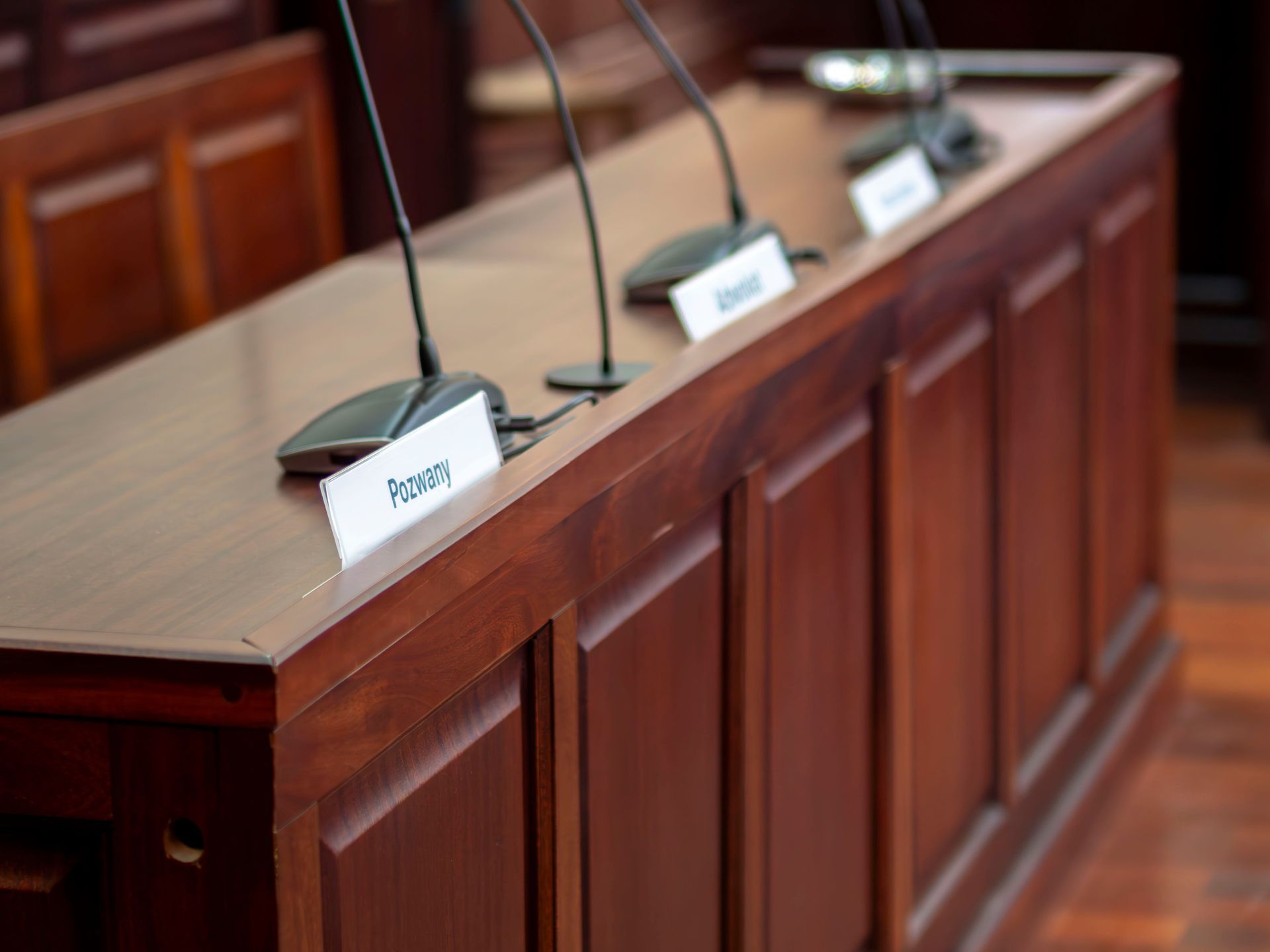 Tribune des témoins vide, avec microphones et plaques nominatives, sur un banc en bois