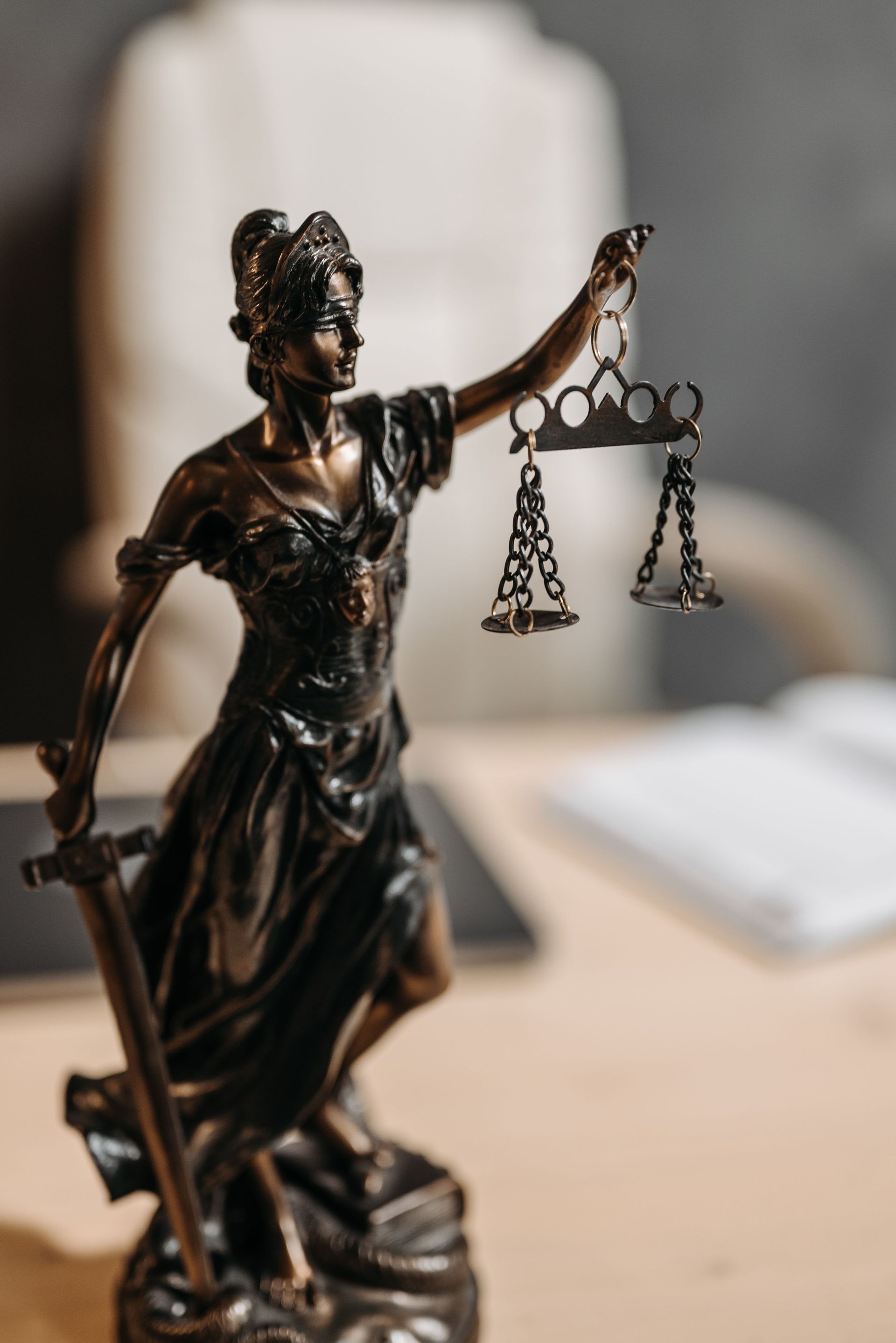 Statuette en bronze de la Dame Justice tenant une balance sur un bureau, avec un carnet flou en arrière-plan.