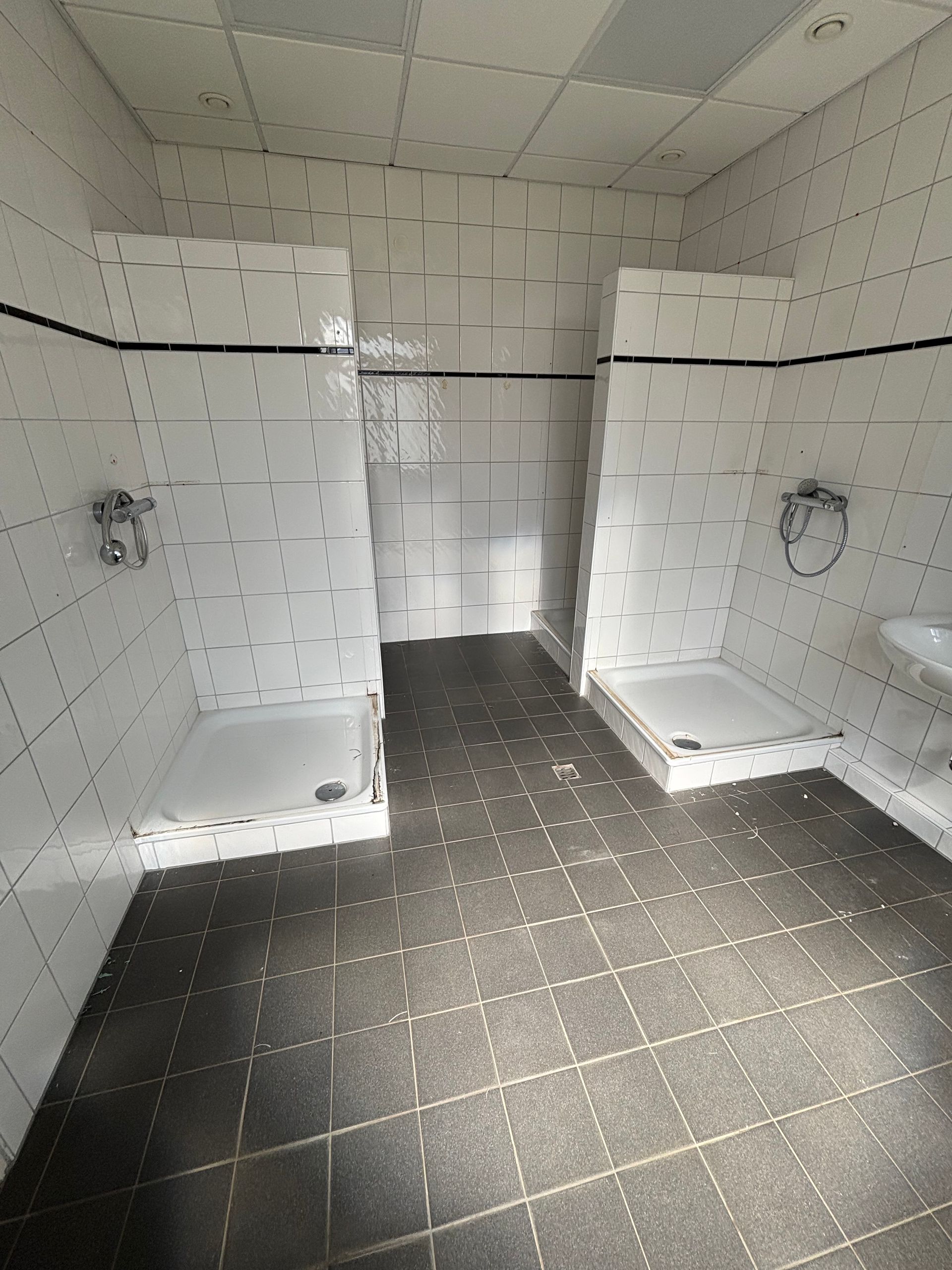 Barrierefreies Duschbad mit zwei gefliesten, ebenerdigen Duschkabinen, weißen Wänden und dunklen Bodenfliesen.
