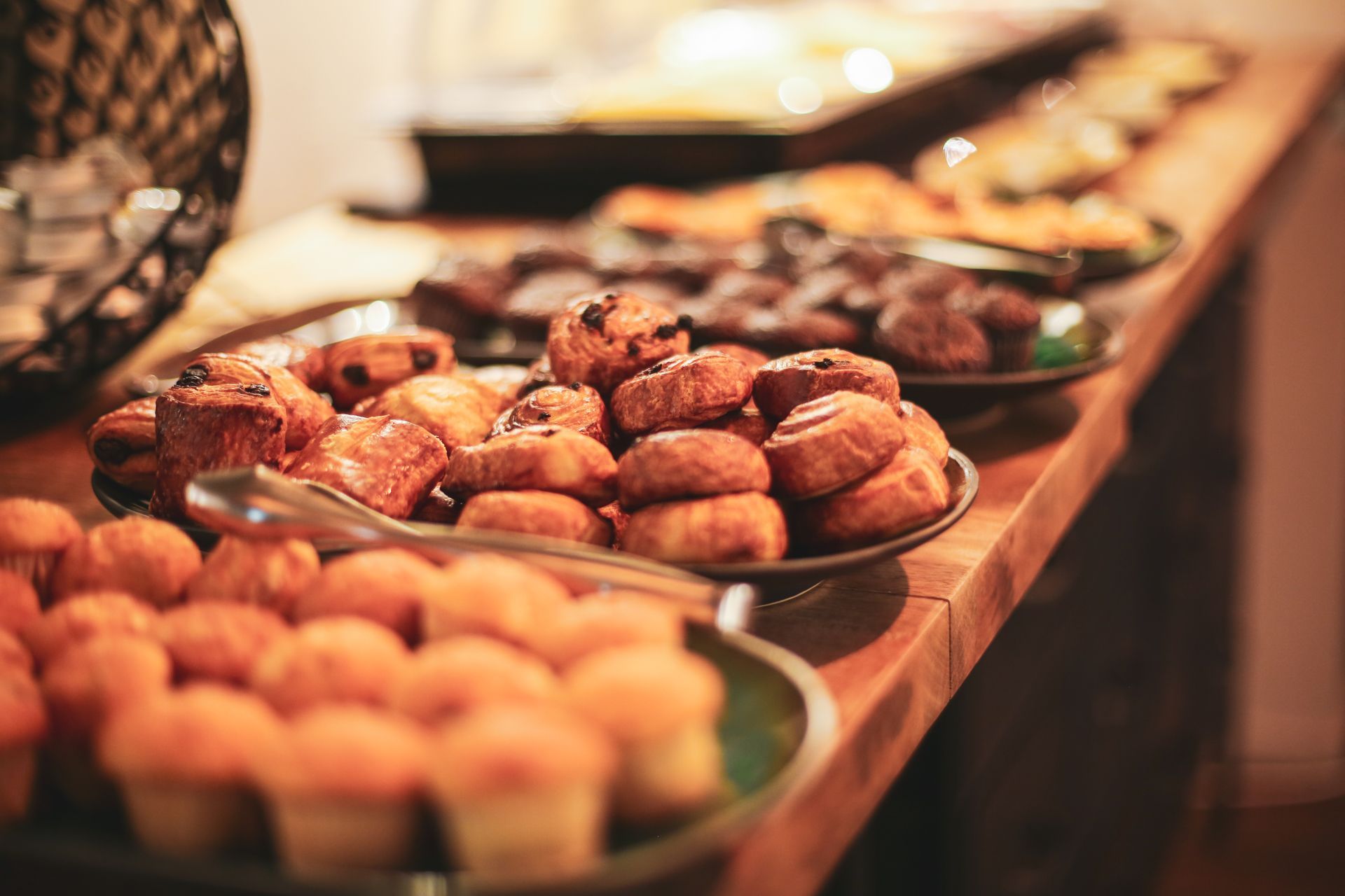 Een close-up van een ontbijtbuffet in Hotel Heemskerk met verschillende soorten vers gebak, waaronder mini-muffins, kaneelbroodjes en chocoladebroodjes, op houten schalen en een houten tafel.