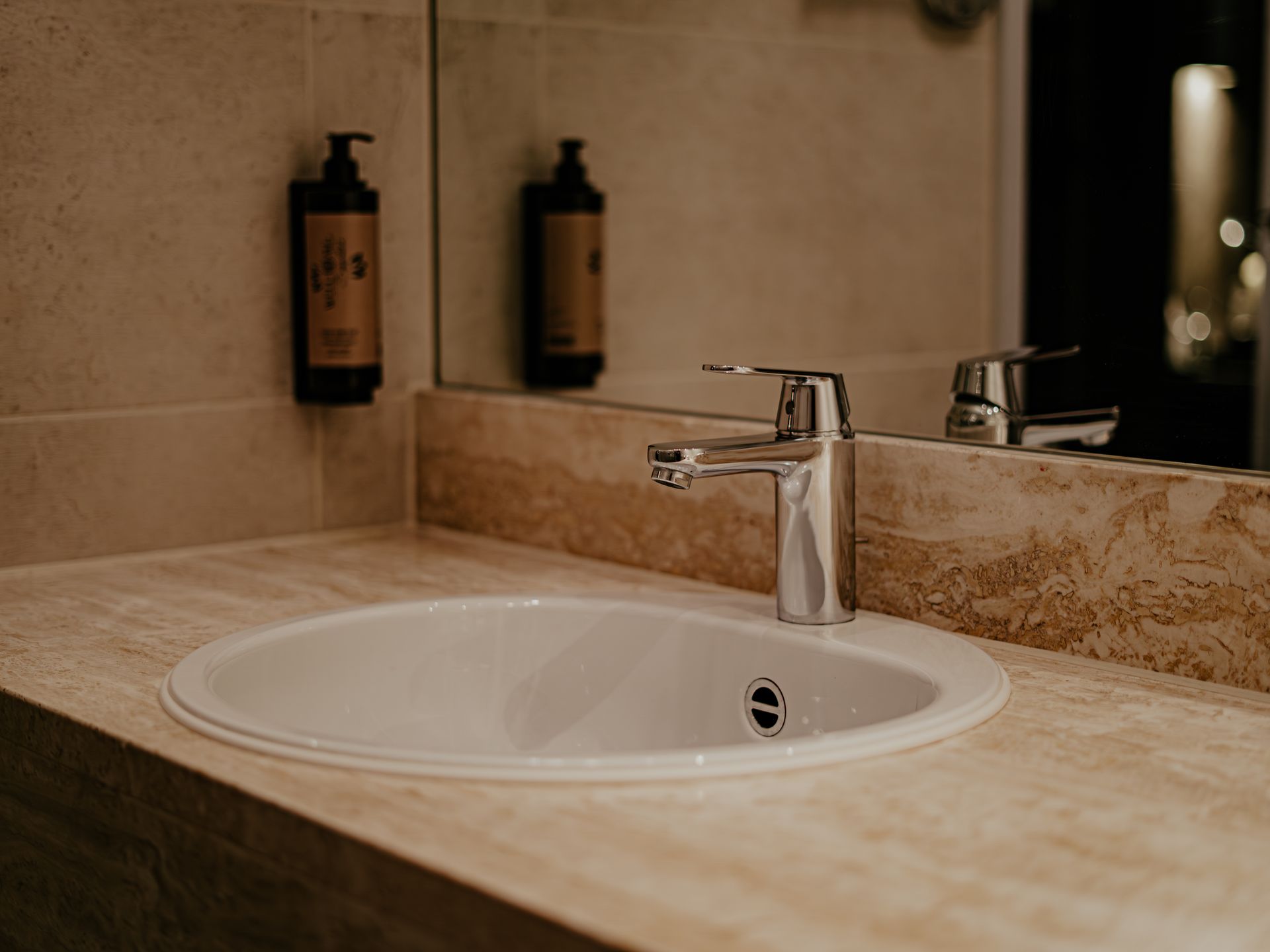 A modern washbasin at Hotel Heemskerk with a chrome faucet and marble countertop; the soap dispenser appears as a reflection in the mirror.