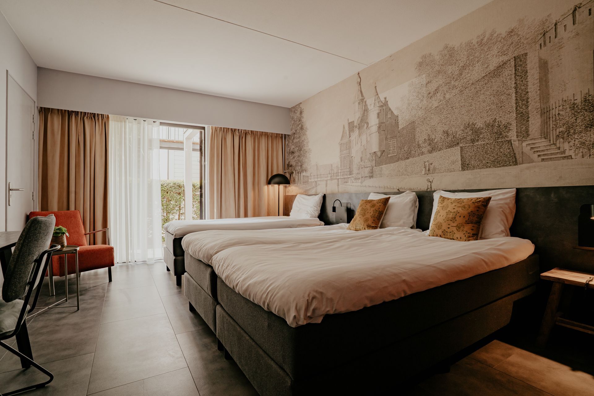 Een hotelkamer met drie bedden, een bureau, stoelen en een groot raam.