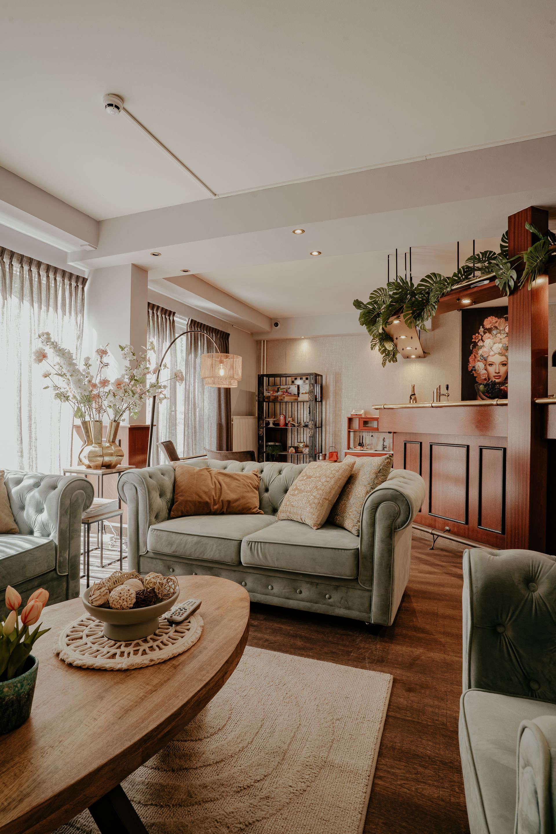 Een overzichtsfoto van de lounge van Hotel Heemskerk, met een grote ovale houten tafel omringd door grijze gestoffeerde stoelen, moderne hanglampen erboven, een zithoek met blauwe en grijze banken in de achtergrond, en houten vloeren door de hele ruimte.