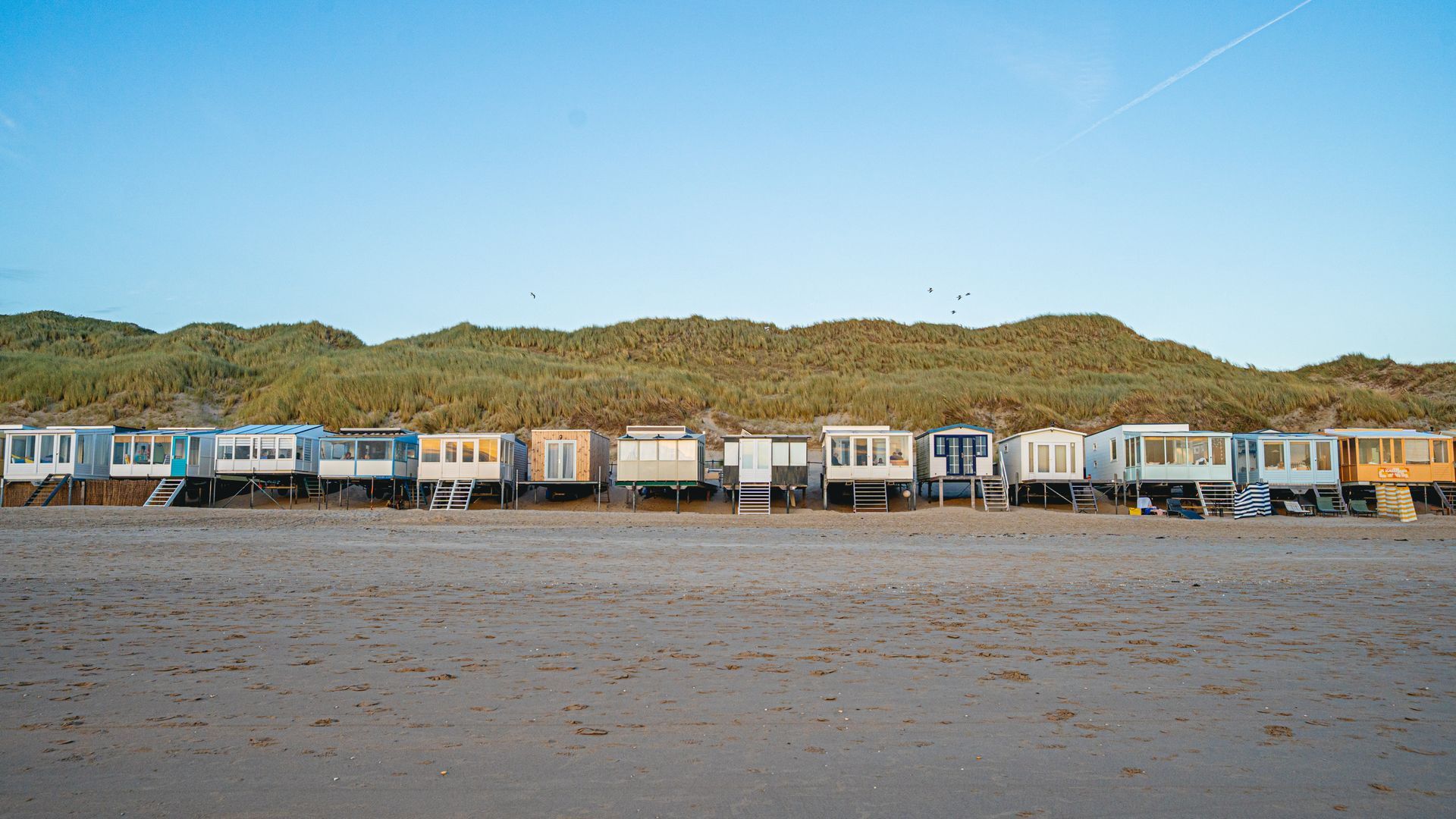 Een vrouw loopt over een zandpad naar het strand.