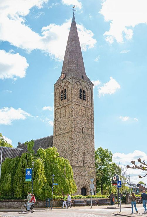 De St. Martinuskerk, prominent aanwezig in het dorpscentrum van Heemskerk, Noord-Holland. De foto toont de markante toren en een deel van het omliggende plein met voetgangers en fietsers.