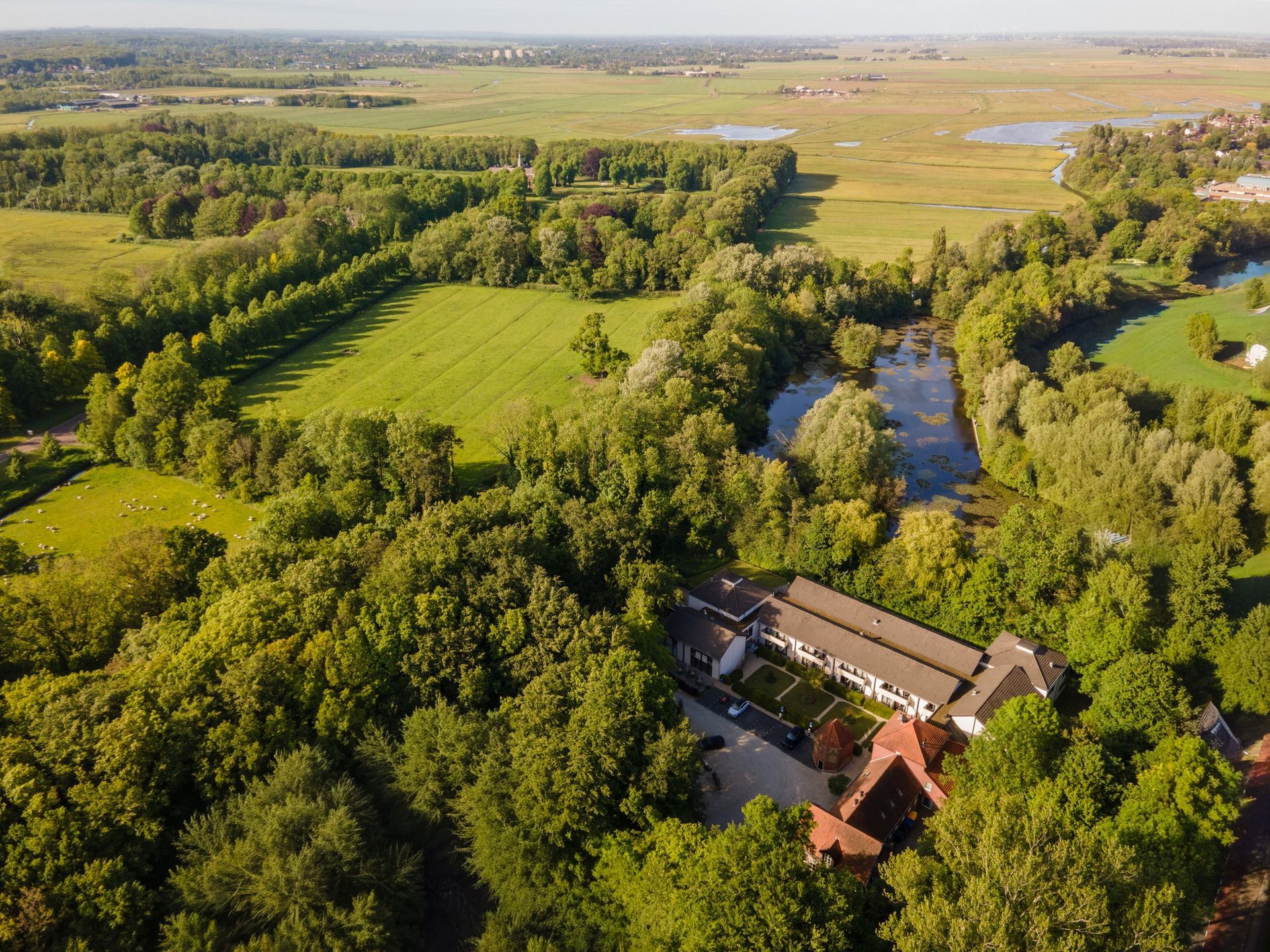 Aerial view of Hotel Heemskerk, surrounded by greenery with a clear view of the buildings, parking area, and wooded surroundings.