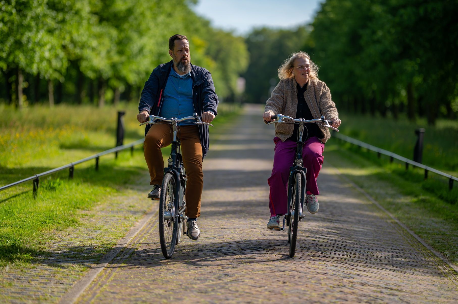 Twee personen fietsen op een geasfalteerd pad dat door een groene, bosrijke omgeving in Heemskerk loopt. Ze fietsen in dezelfde richting, weg van de camera.