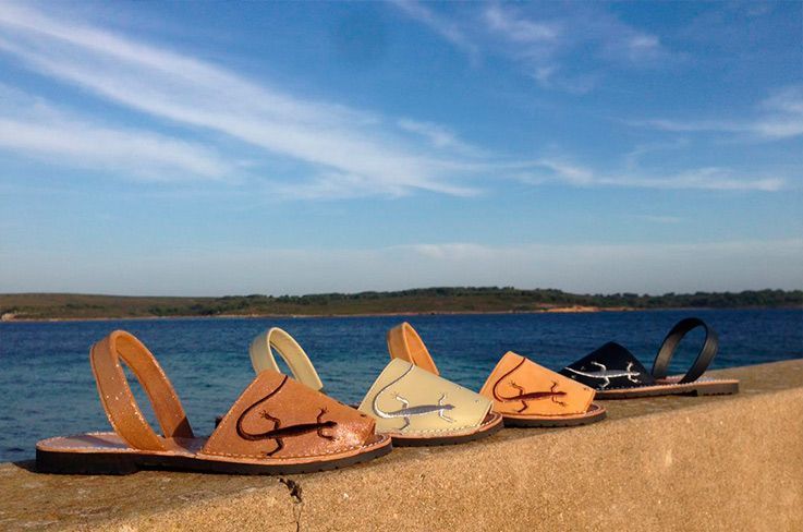 Three pairs of sandals are lined up on a wall near the ocean