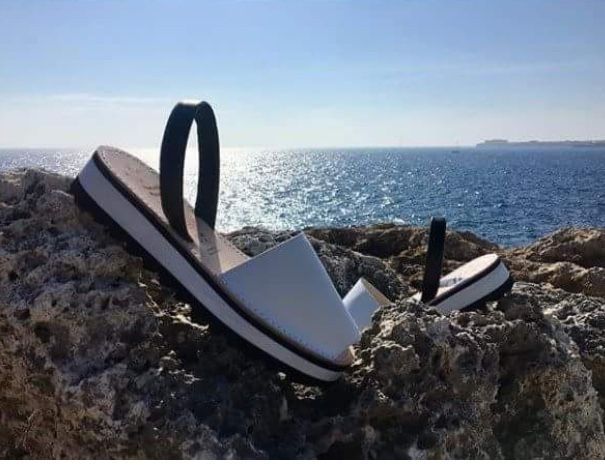 A pair of white sandals are sitting on a rock near the ocean