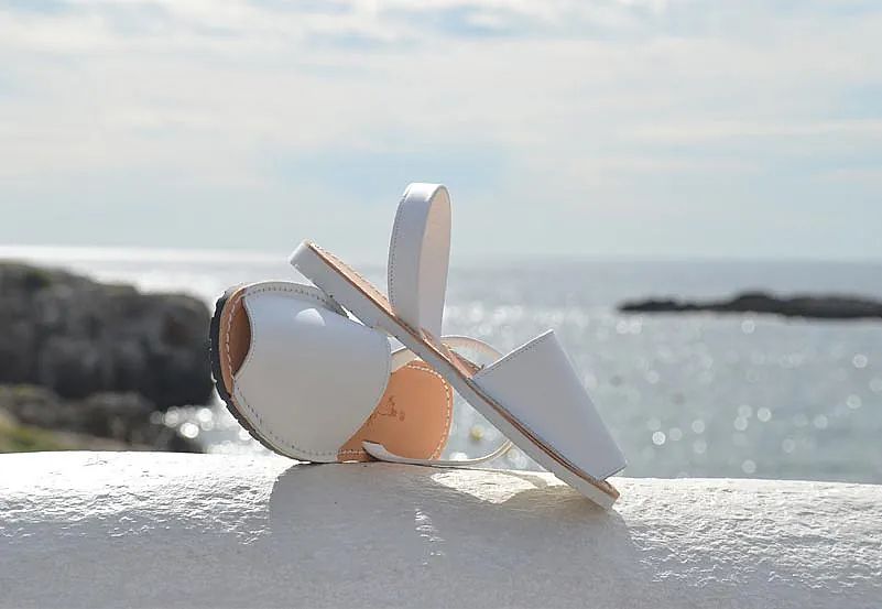 A pair of white sandals sitting on top of a white wall with the ocean in the background.