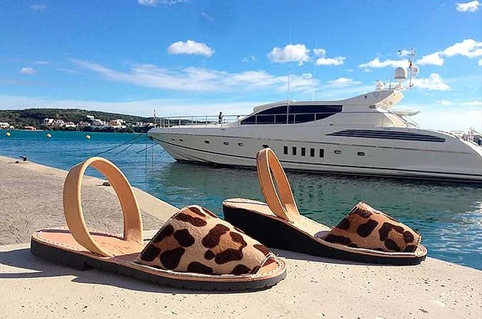 Un par de sandalias con estampado de leopardo se encuentran en un muelle junto a un barco.