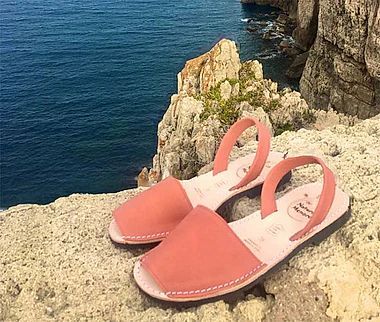 A pair of pink sandals are sitting on a rock near the ocean.
