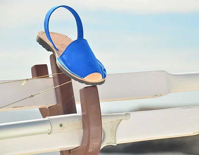 A blue sandal is sitting on top of a wooden railing.