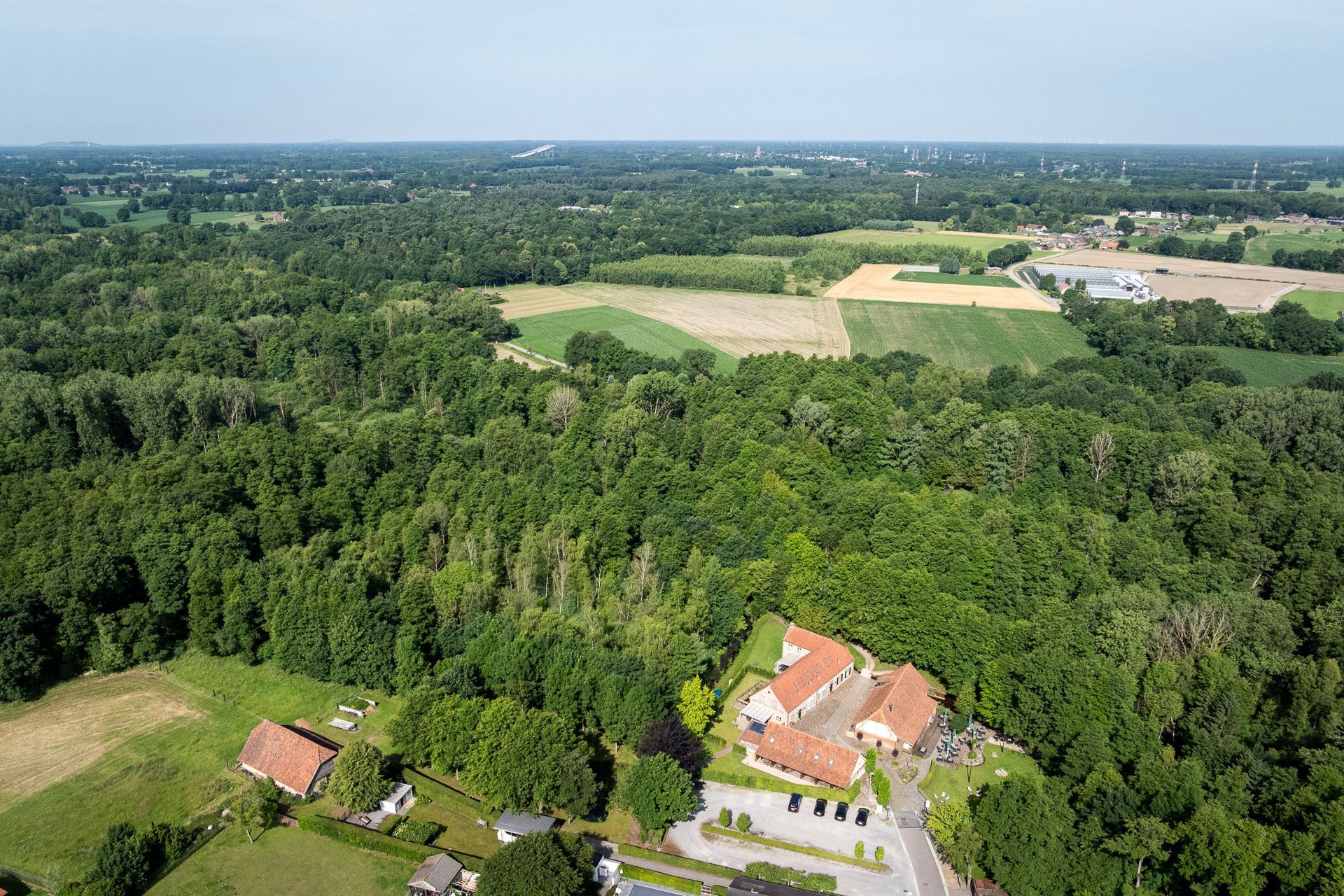 Luchtfoto van gebouwen verscholen in een weelderig groen bos met velden op de achtergrond.