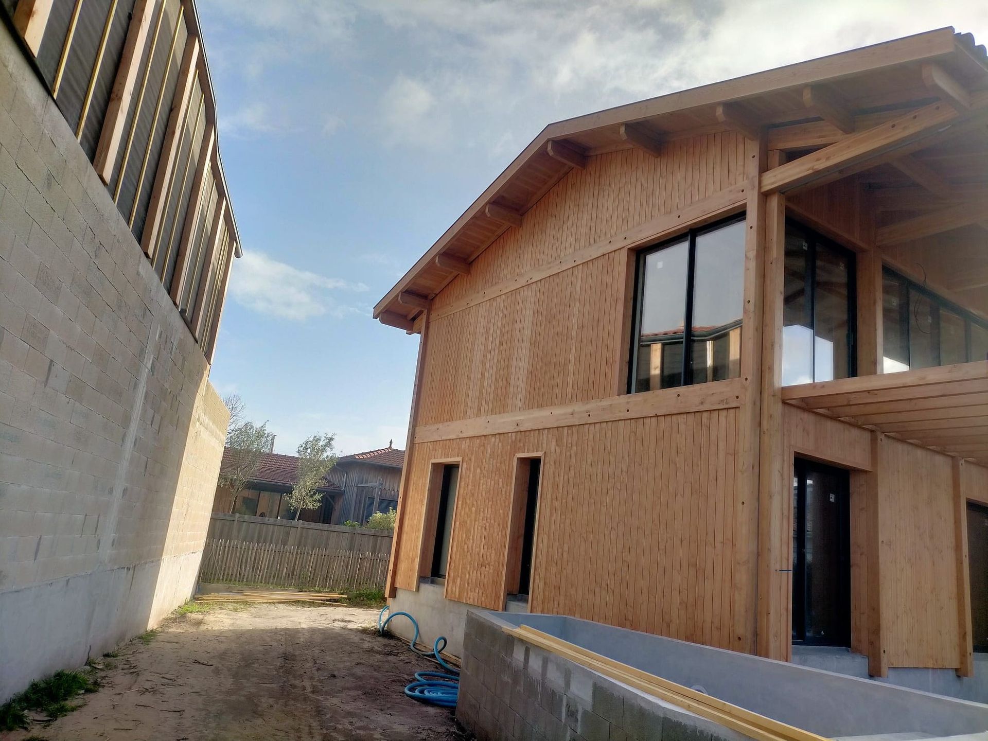 Un mur de pierre à gauche et une maison couverte par du bardage en bois à droite