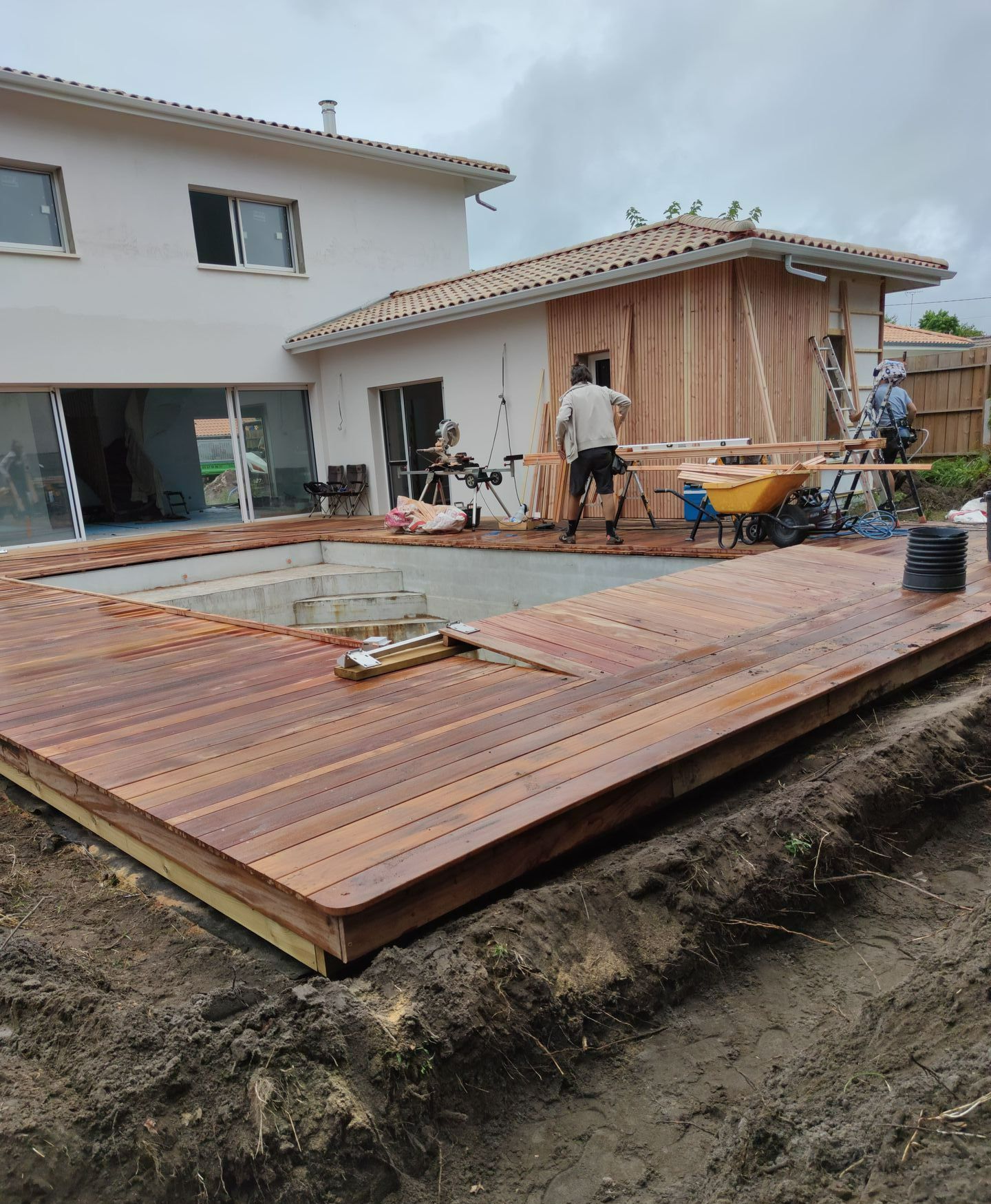 Un chantier d'installation de bardage et d'une terrasse en bois autour d'une piscine