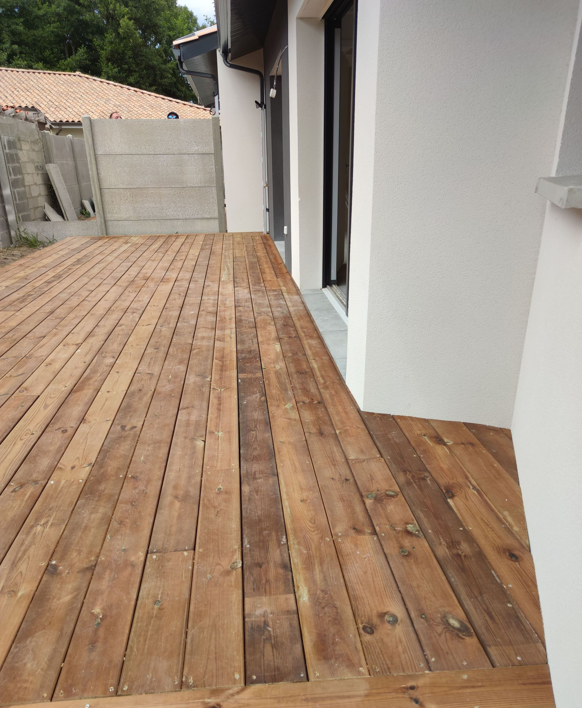 Une terrasse en bois bordé par un mur blanc 