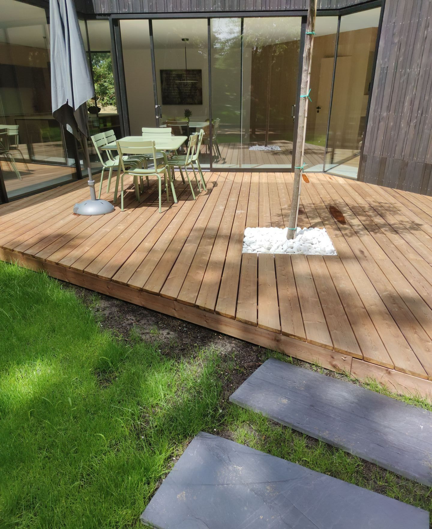 Une terrasse en bois avec un arbre et une table verte