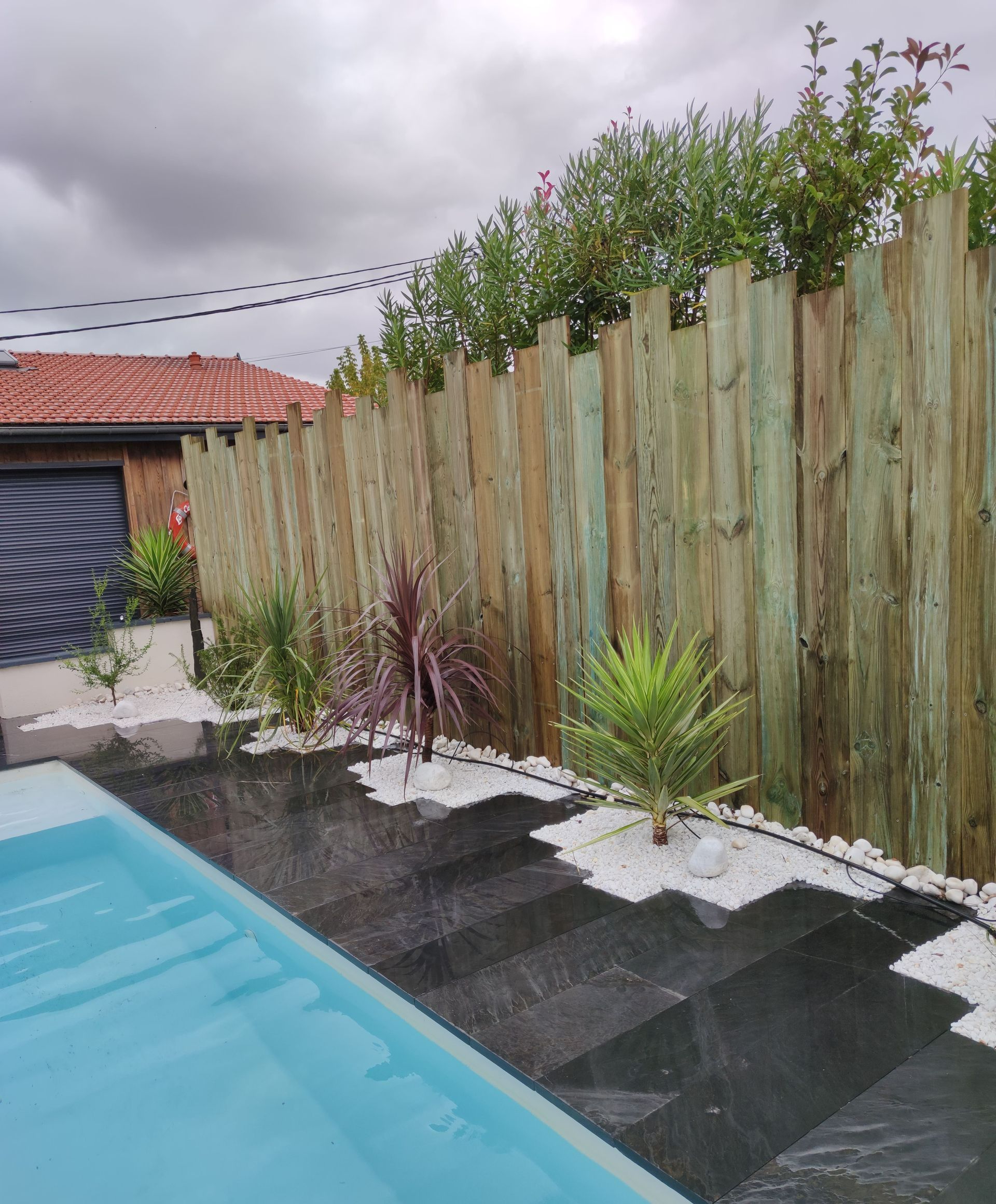 Des plantes le long d'une barrière en bois avec du carrelage noir