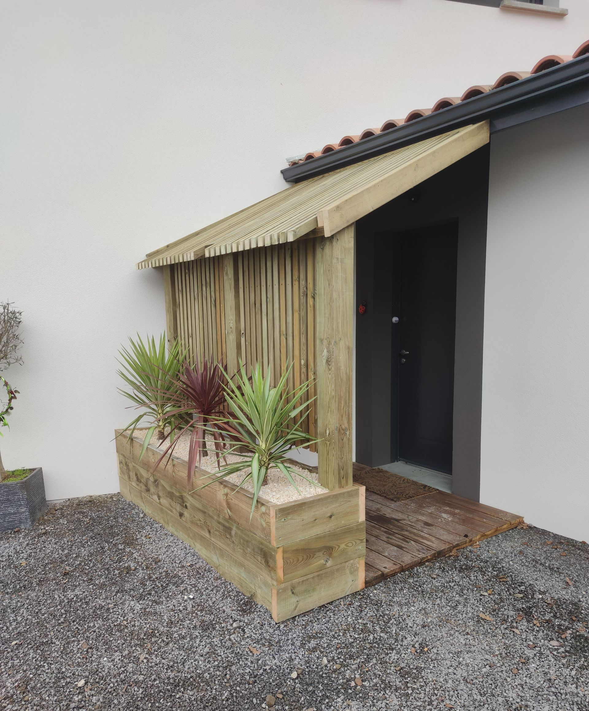 Une entrée protégée par une structure en bois avec une jardinière et des plantes
