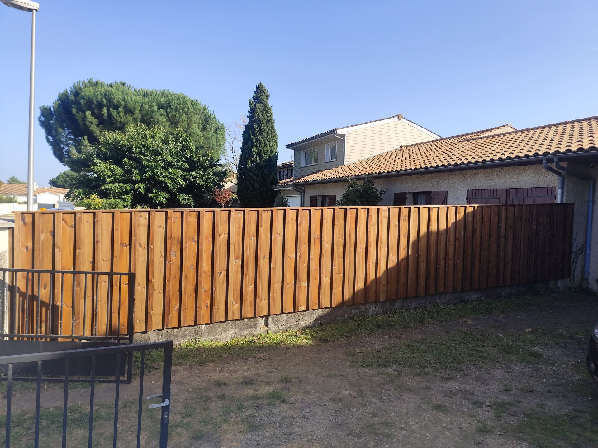 Une clôture en bois avec des pins et une maison derrière
