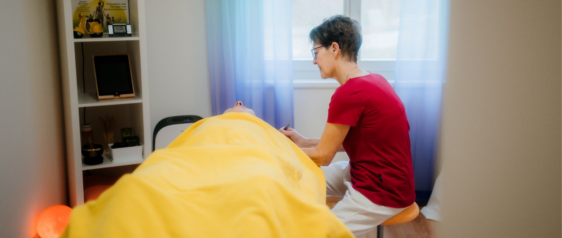 Hände massieren den oberen Rücken und die Schulter einer Person. Ein Handtuch liegt unter dem Kopf.