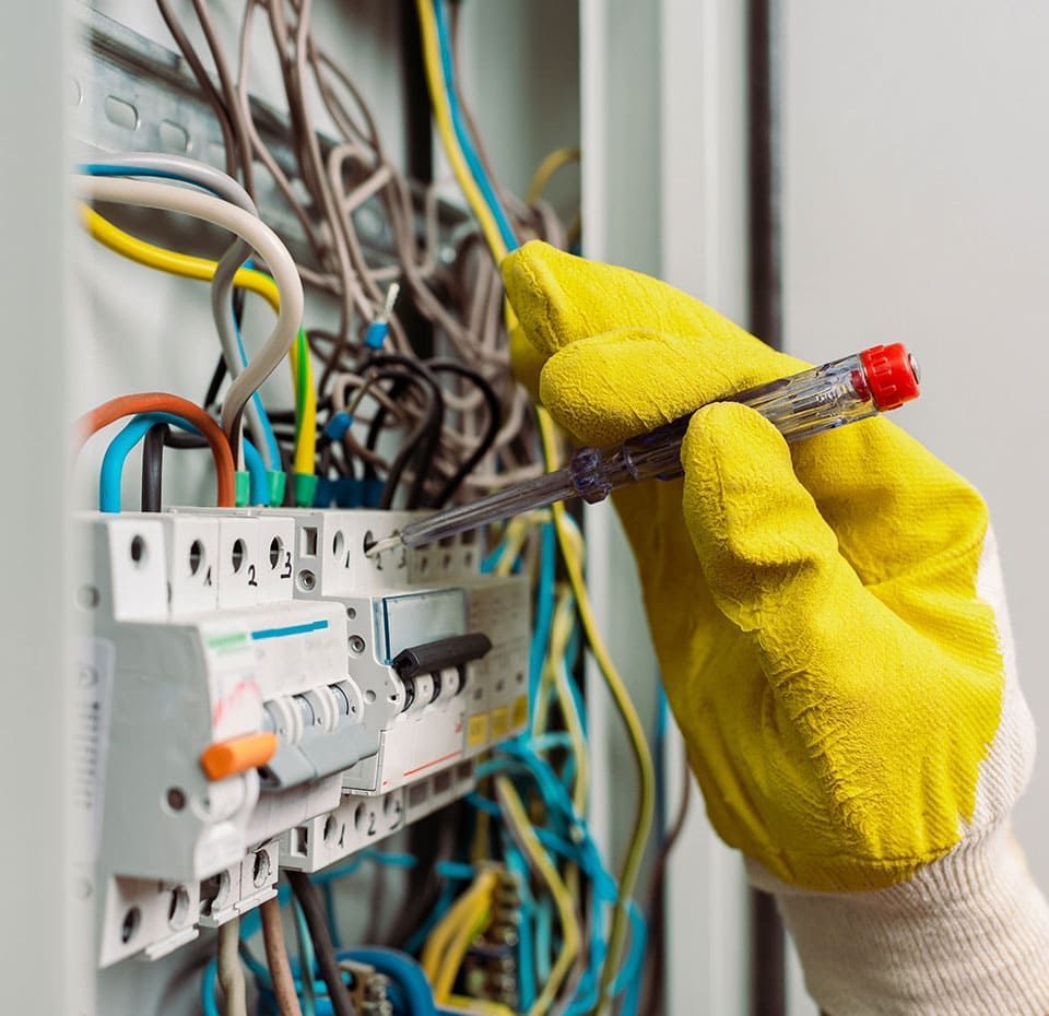 Main ganté tenant un tournevis sur un disjonteur.