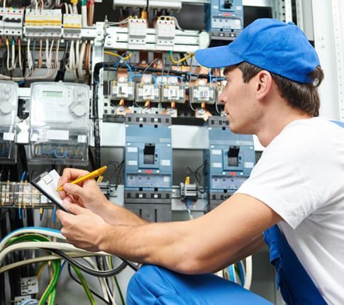 Un électricien en train d'écrire sur un bloc note devant un système électrique