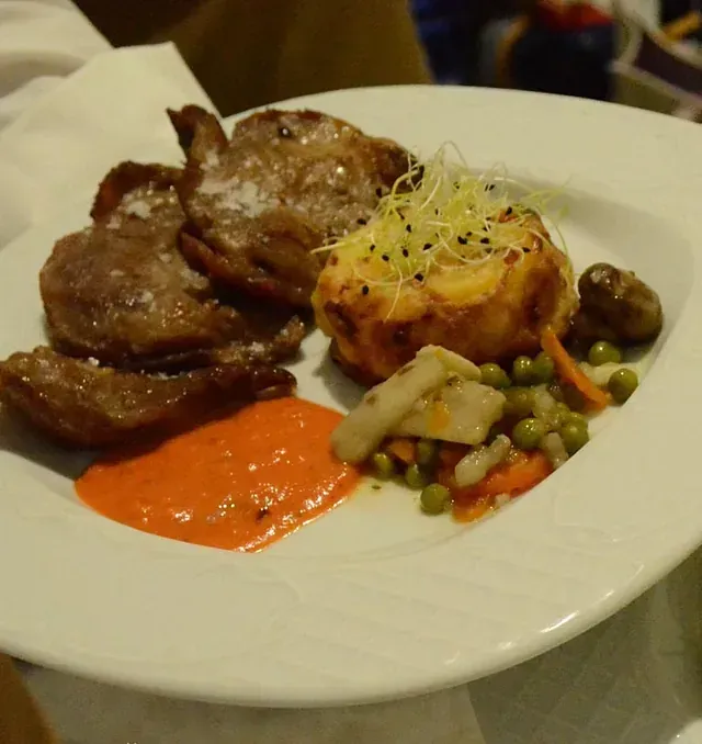 Un plato blanco cubierto con carne y verduras sobre una mesa.