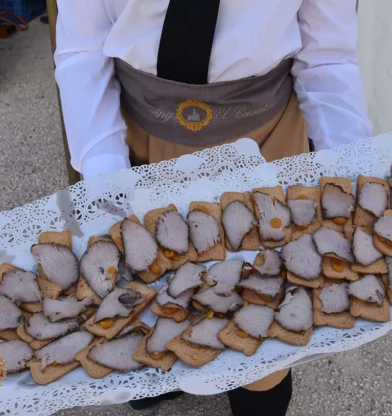Una persona sosteniendo una bandeja con carne cortada en rodajas y galletas