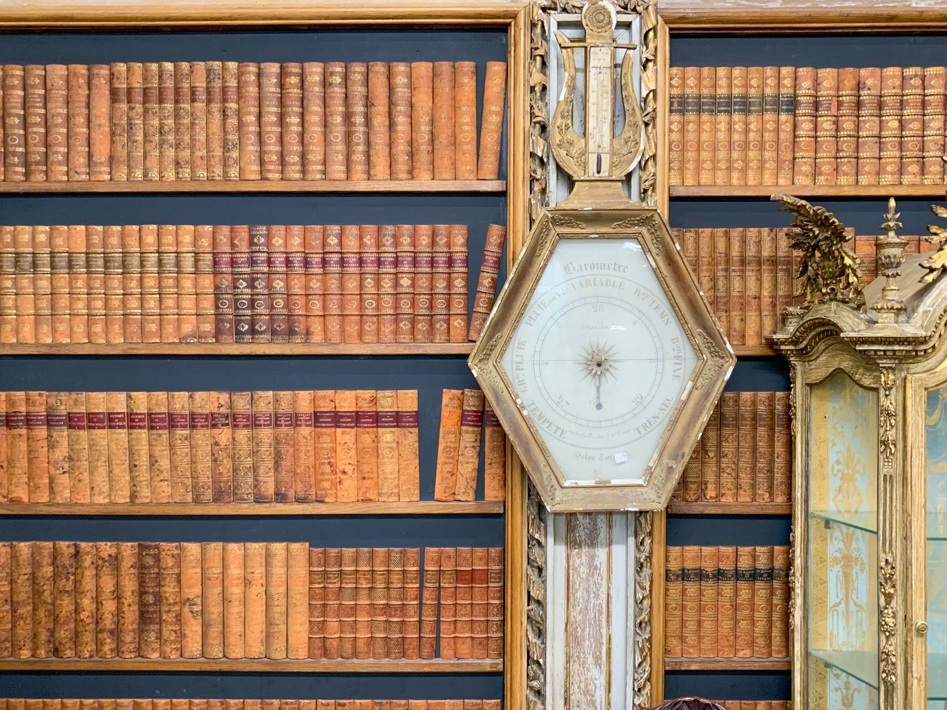 Grande bibliothèque murale avec des anciens livres et une horloge devant.