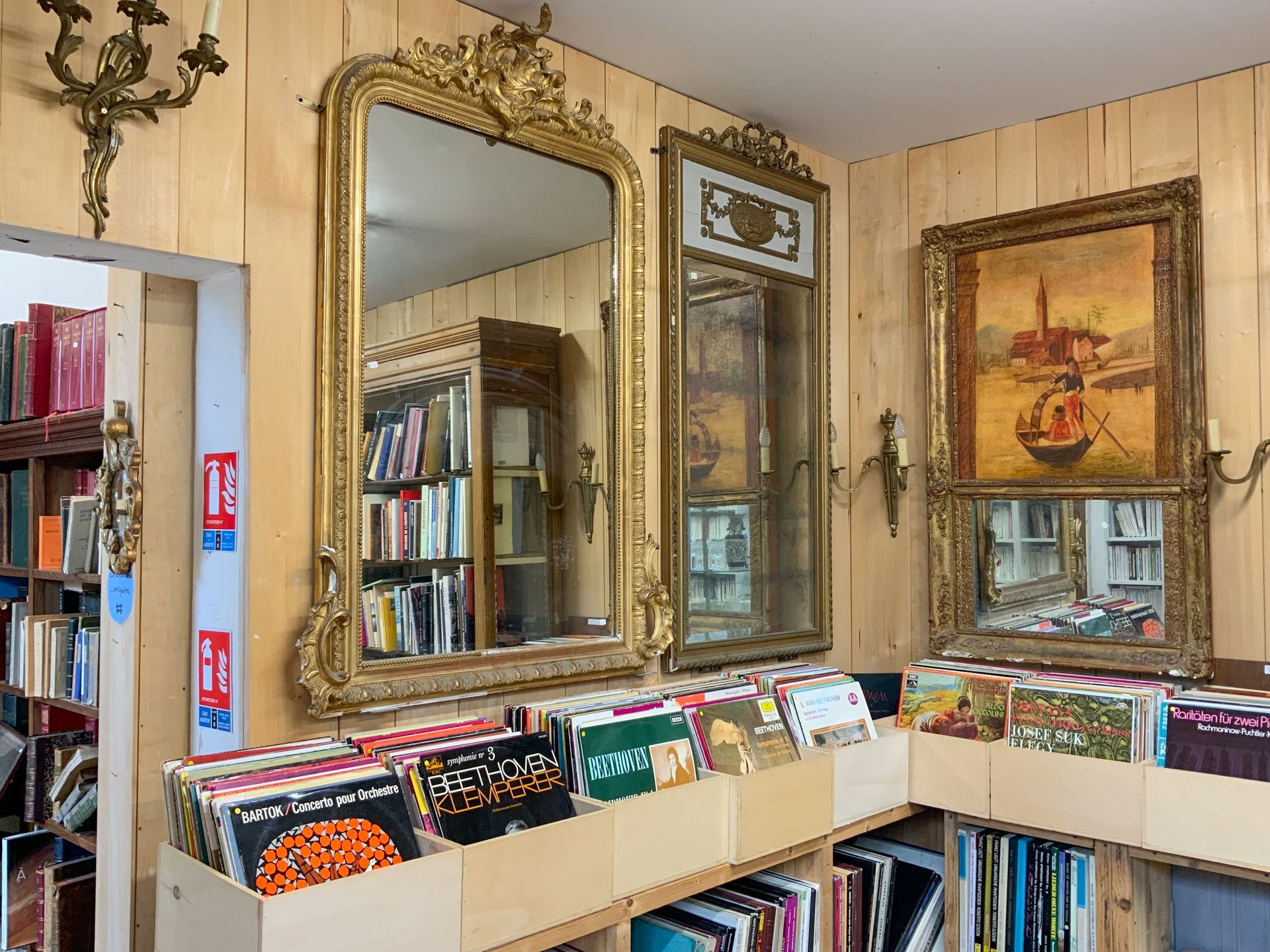 Plusieurs miroirs et tableaux accrochés au mur au-dessus de livres.