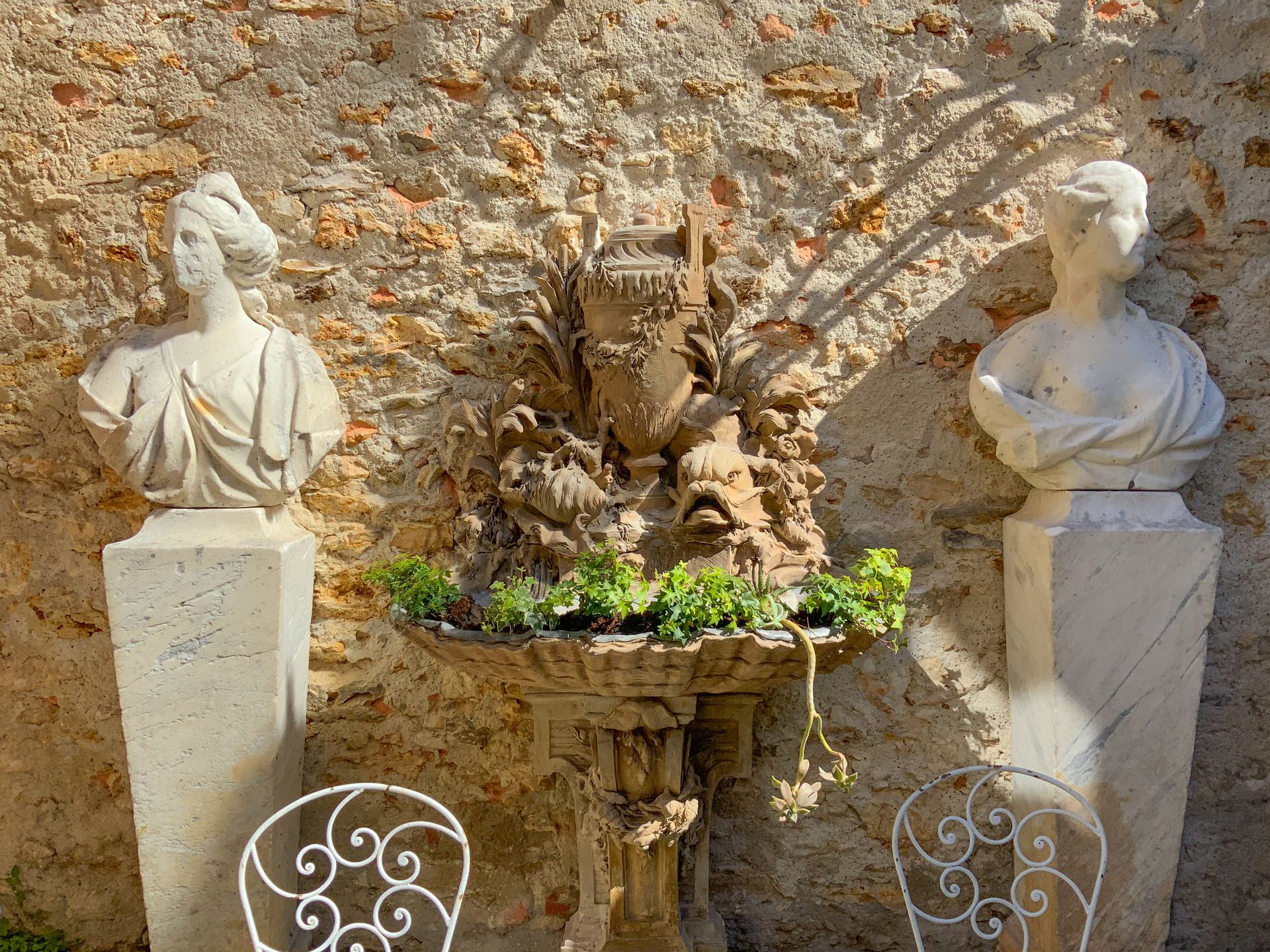 Ancienne fontaine en pierre au milieu de 2 sculptures de bustes.