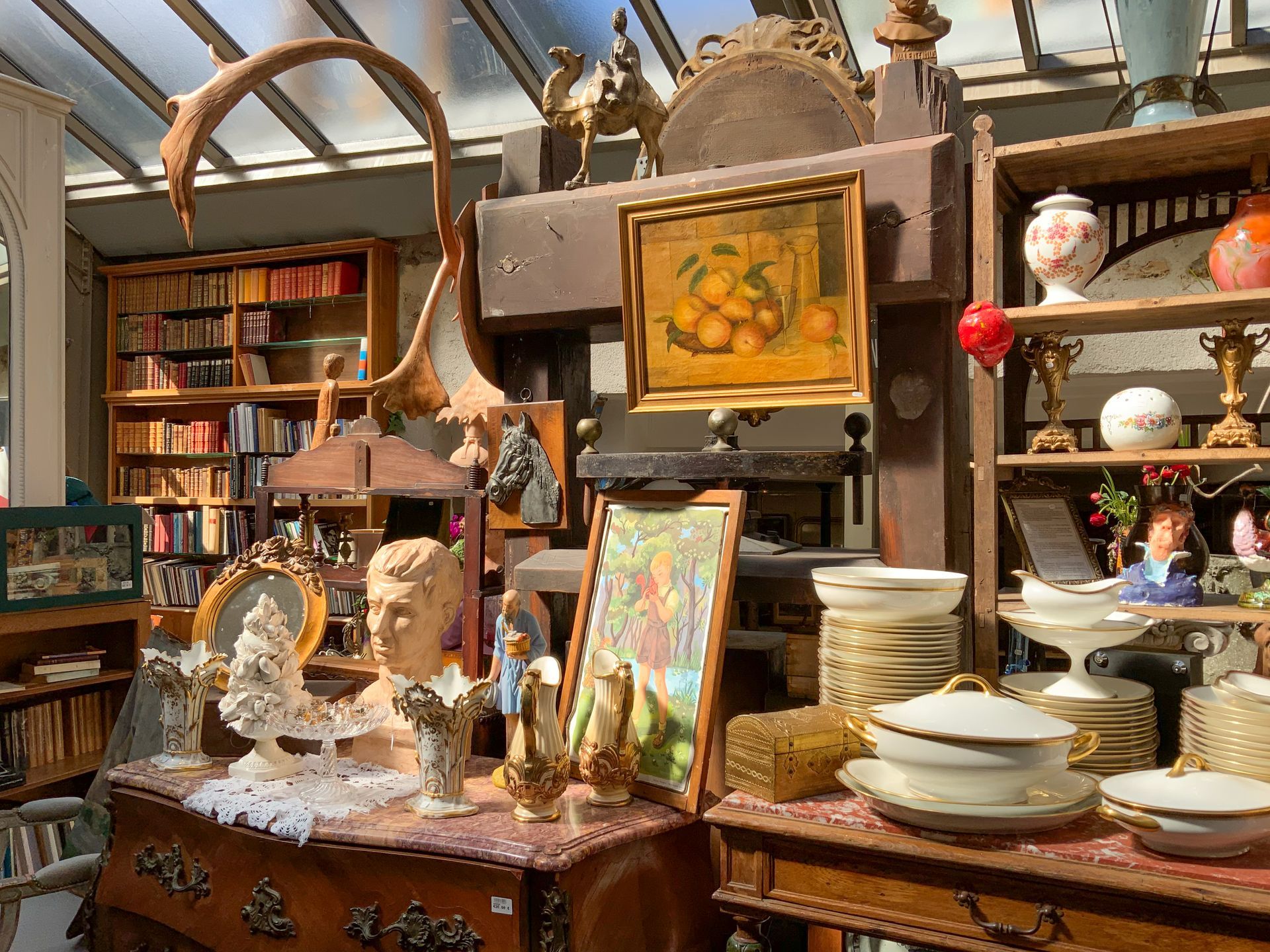 Exposition de vaisselles et bibelots sous une peinture de fruits.