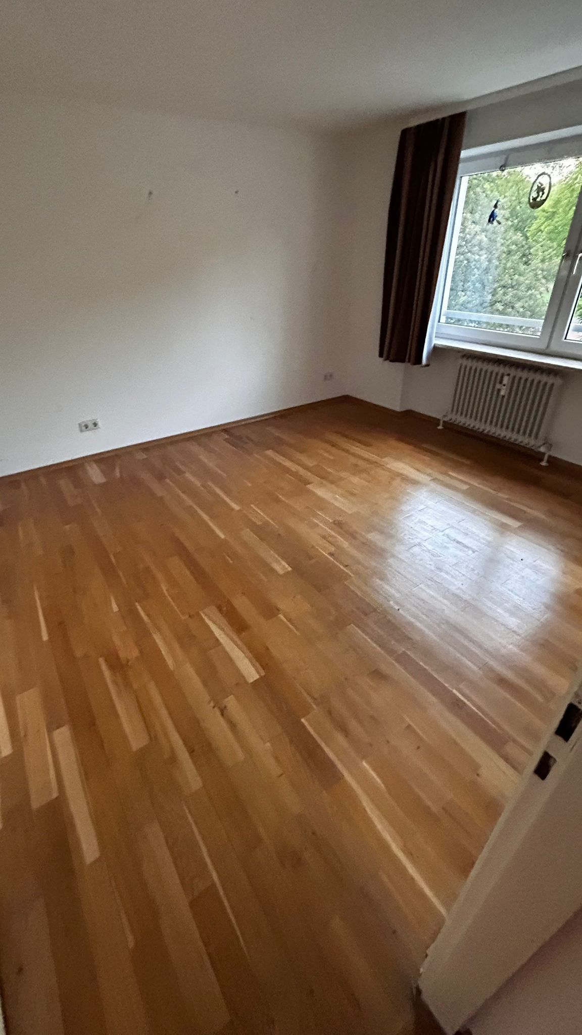 Eine leere Ecke eines Raumes mit einem Fenster und braunen Vorhängen.