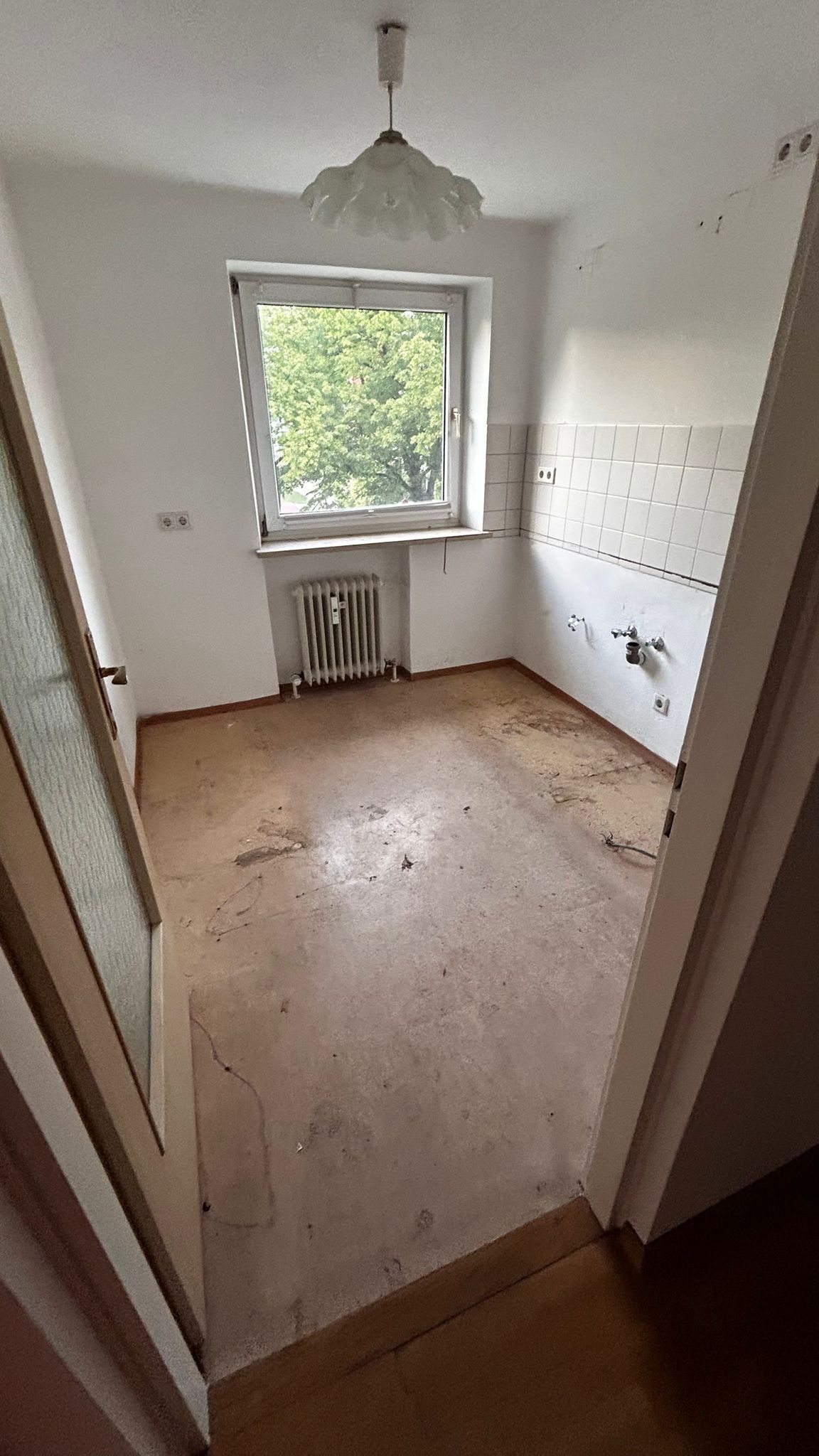 Blick aus einem Fenster auf grüne Bäume in einem weißen Raum mit Deckenlampe.