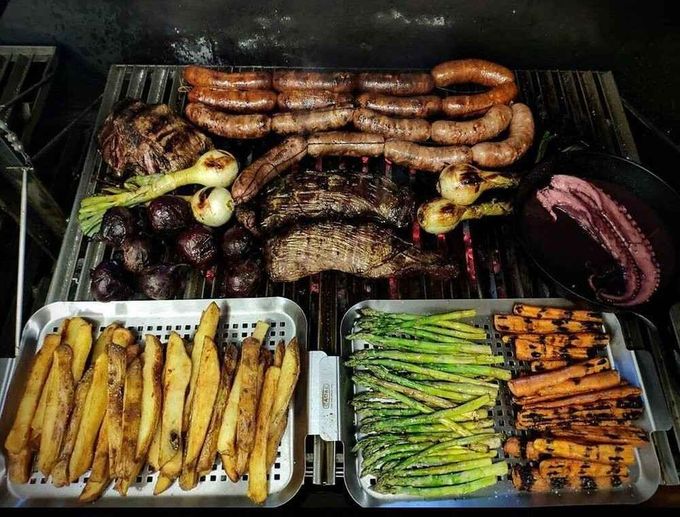 Parrilla cargada de salchichas, costillas, verduras y maíz cocinándose a la brasa.