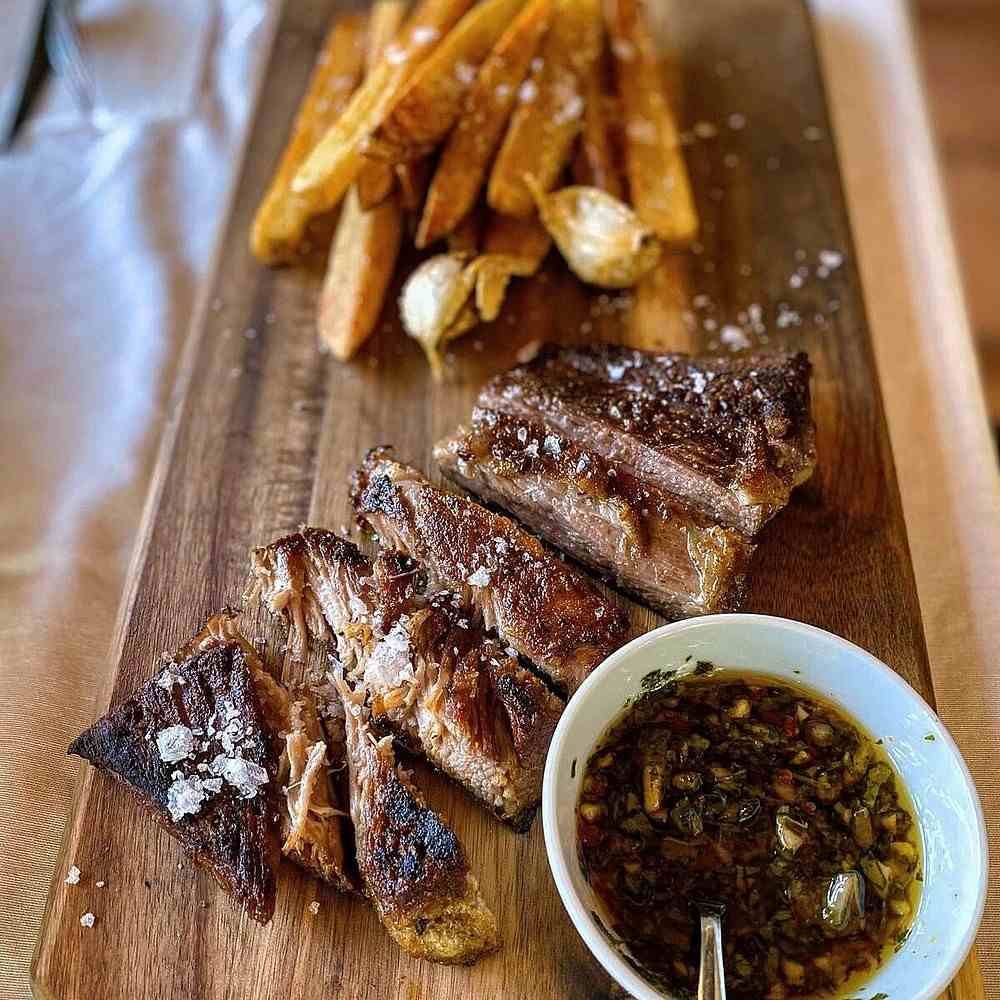 Filete a la parrilla en rodajas con patatas fritas sazonadas y un cuenco de salsa para mojar en una tabla de madera.