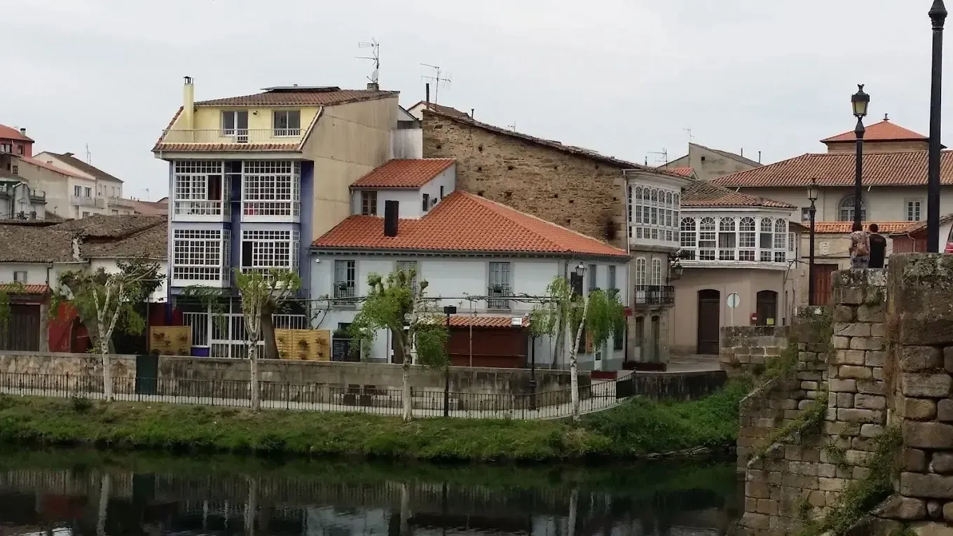 Edificios con diferentes estilos arquitectónicos a lo largo de la orilla de un río bajo un cielo nublado.