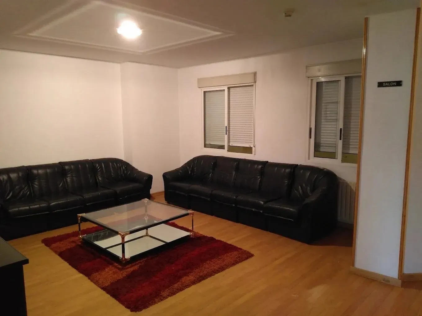 Sala de estar con dos sofás de cuero negro, mesa de café y ventanas.