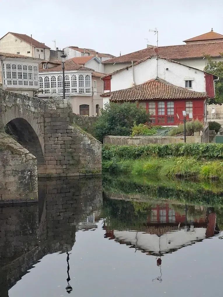 Arco de puente de piedra sobre aguas tranquilas, que refleja edificios 