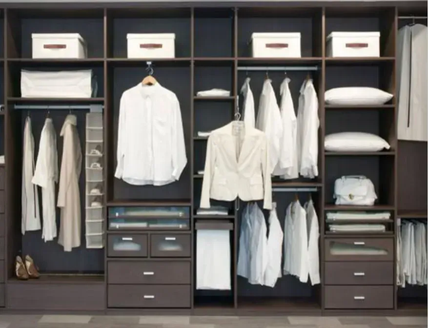 Armario empotrado con vestidor, cajones, estantes y almohadas para camisas blancas, todo en un armario de madera oscura.