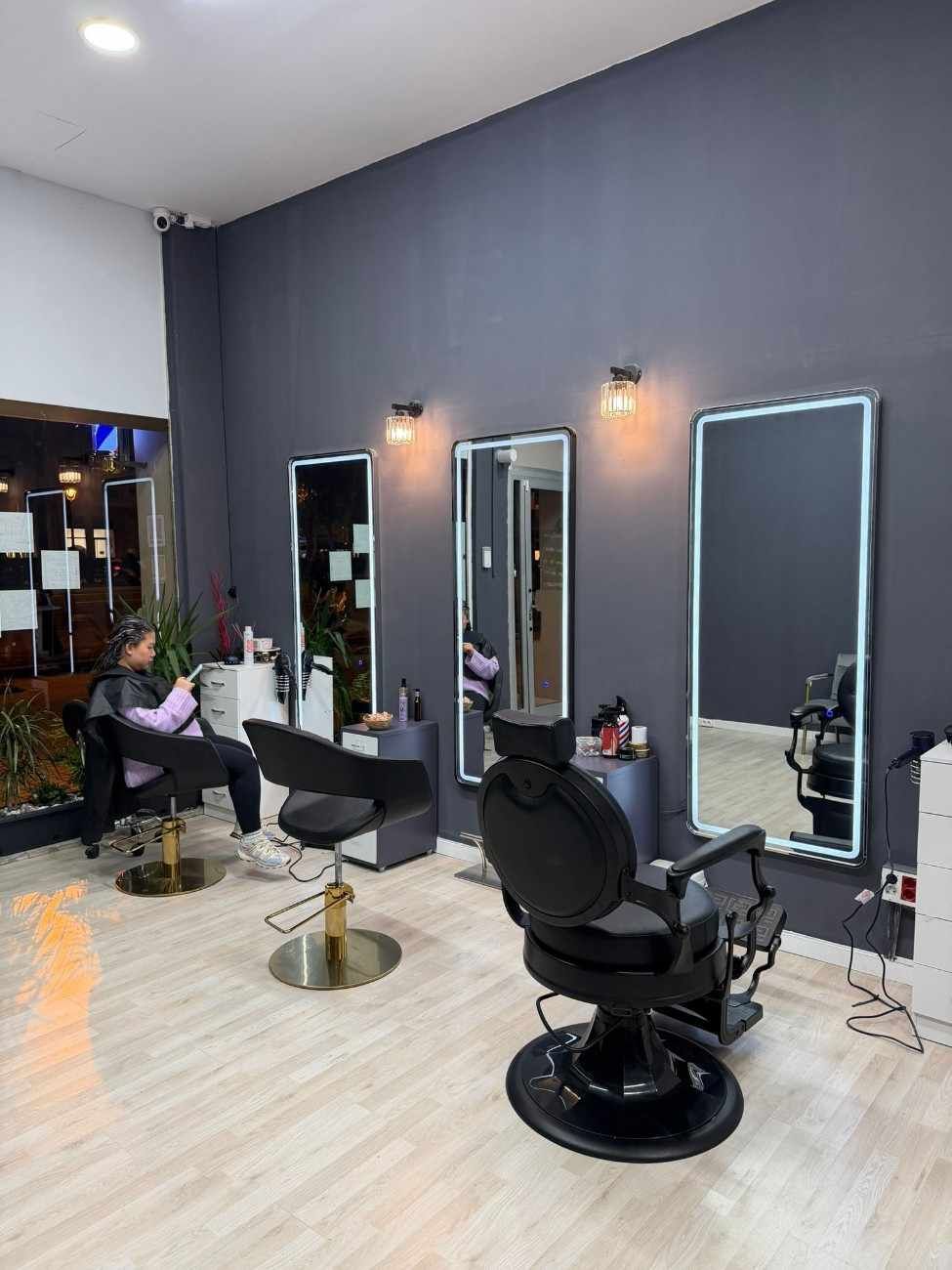 Interior de peluquería con tres espejos, sillas y una clienta peinándose.