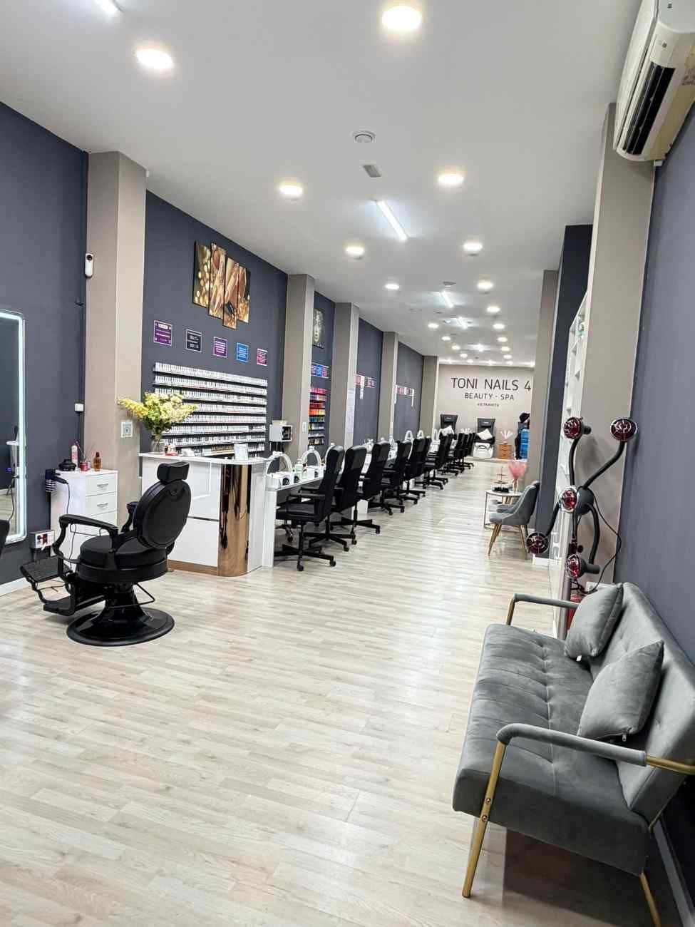 Interior de salón de uñas con filas de estaciones, paredes gris oscuro, detalles en blanco.