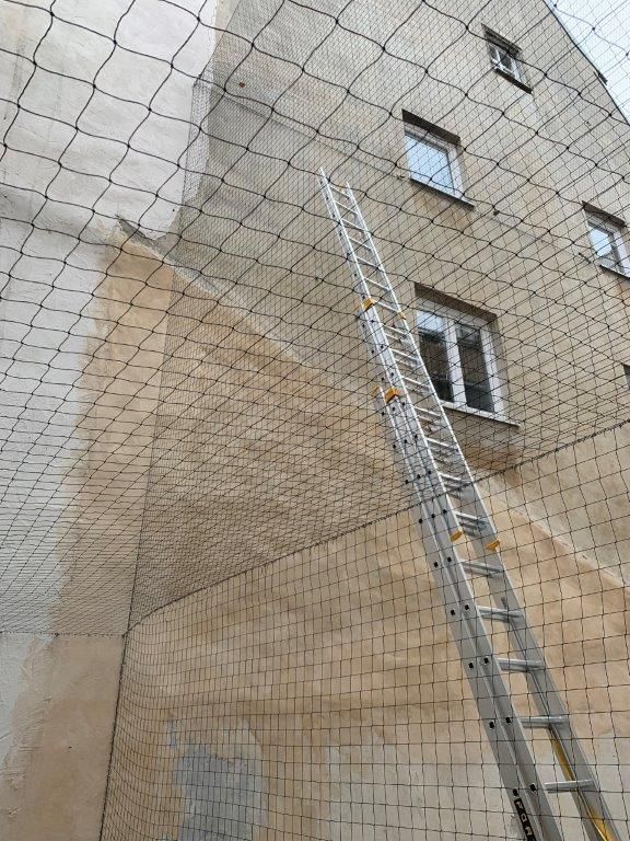 Ein an der Fassade eines Gebäudes angebrachtes Sicherheitsnetz, an dem eine Leiter lehnt.